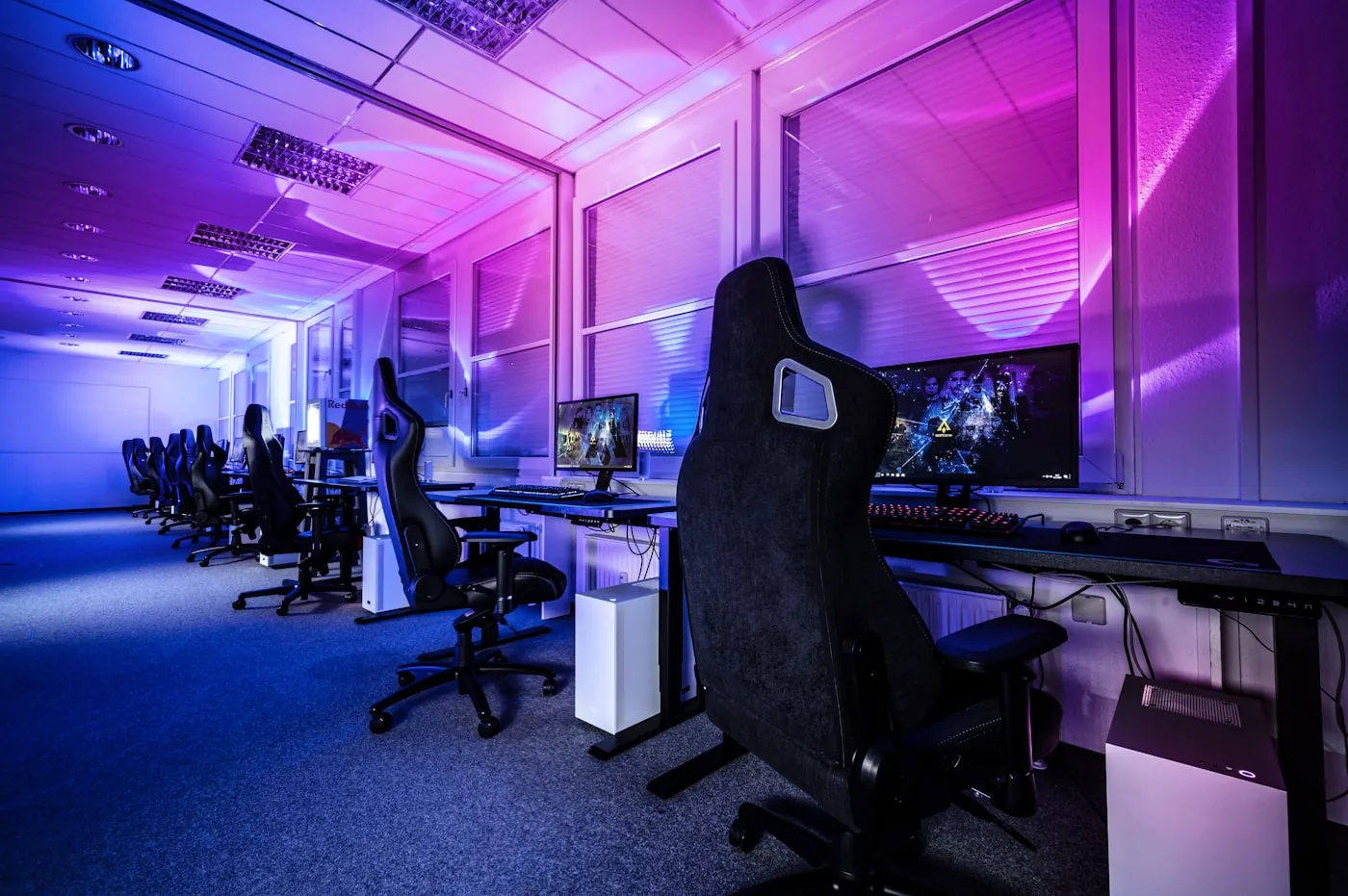 An esports lounge bathed in pink and purple light, rows of gaming stations ready for players