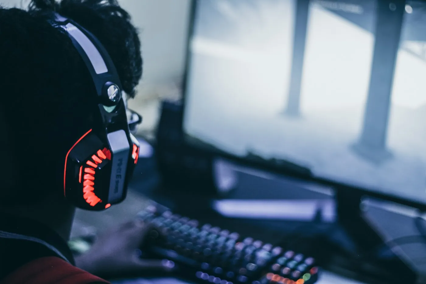 A gamer in a red-lit headset at a keyboard, dialed into the screen
